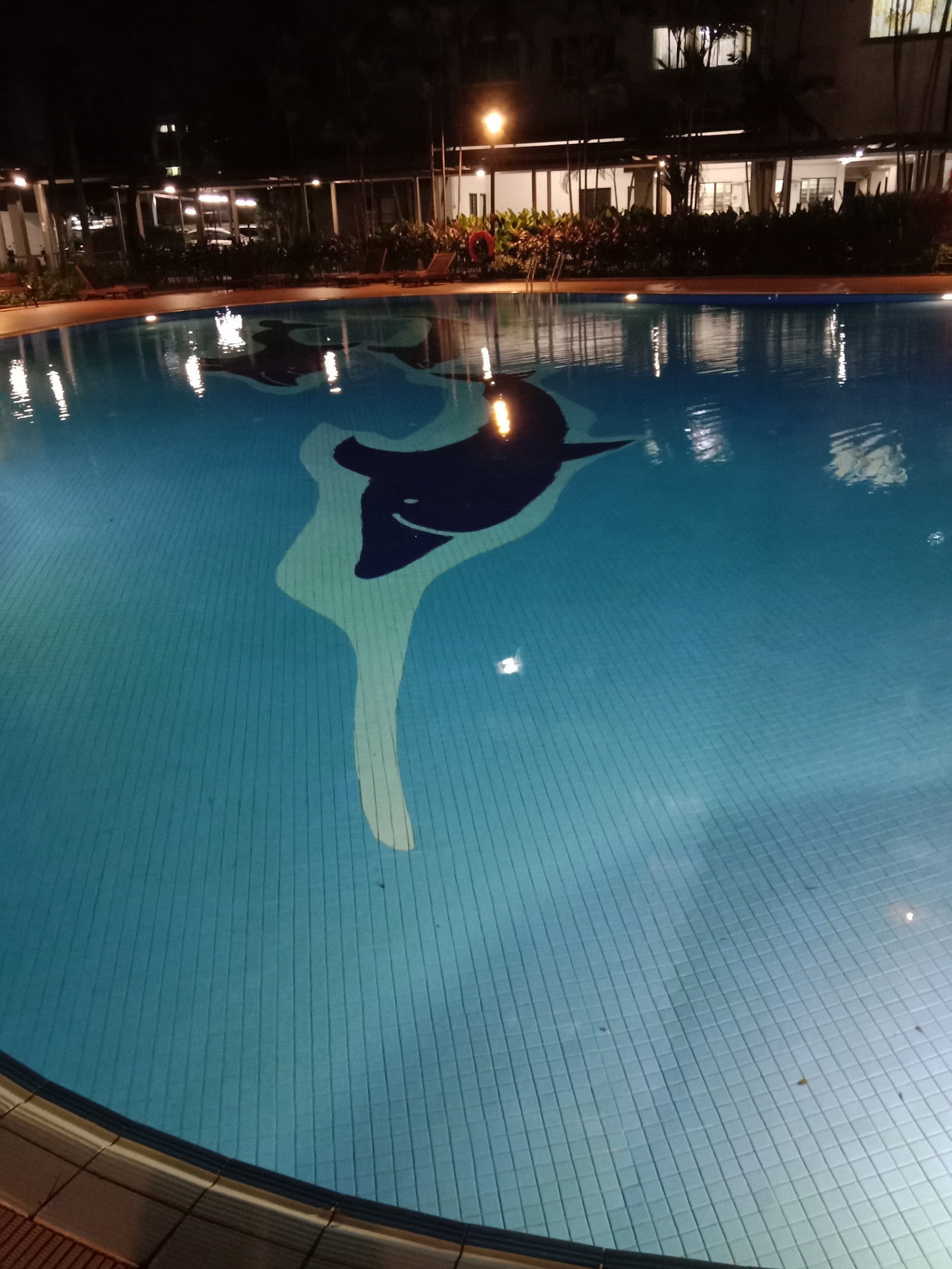 Puncak Damansara: Nighttime swimming pool with a dolphin tile mosaic on the pool floor, surrounded by loungers and a lit building in background