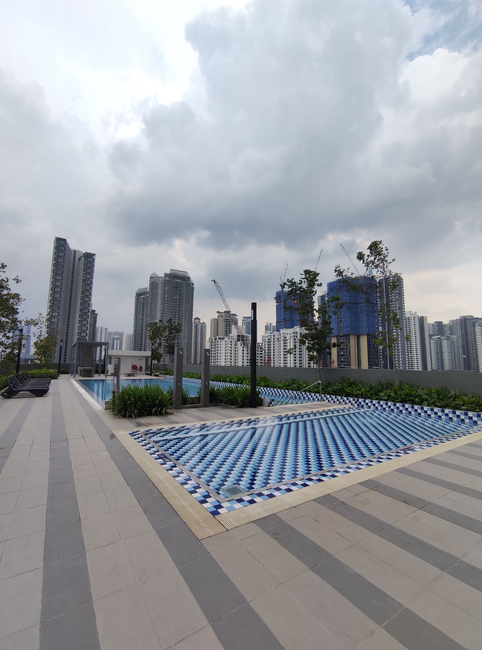 Kiara Kasih: Rooftop swimming pool with tiled deck and mosaic-patterned pool floor, overlooking city skyline with high-rise buildings and construction cranes