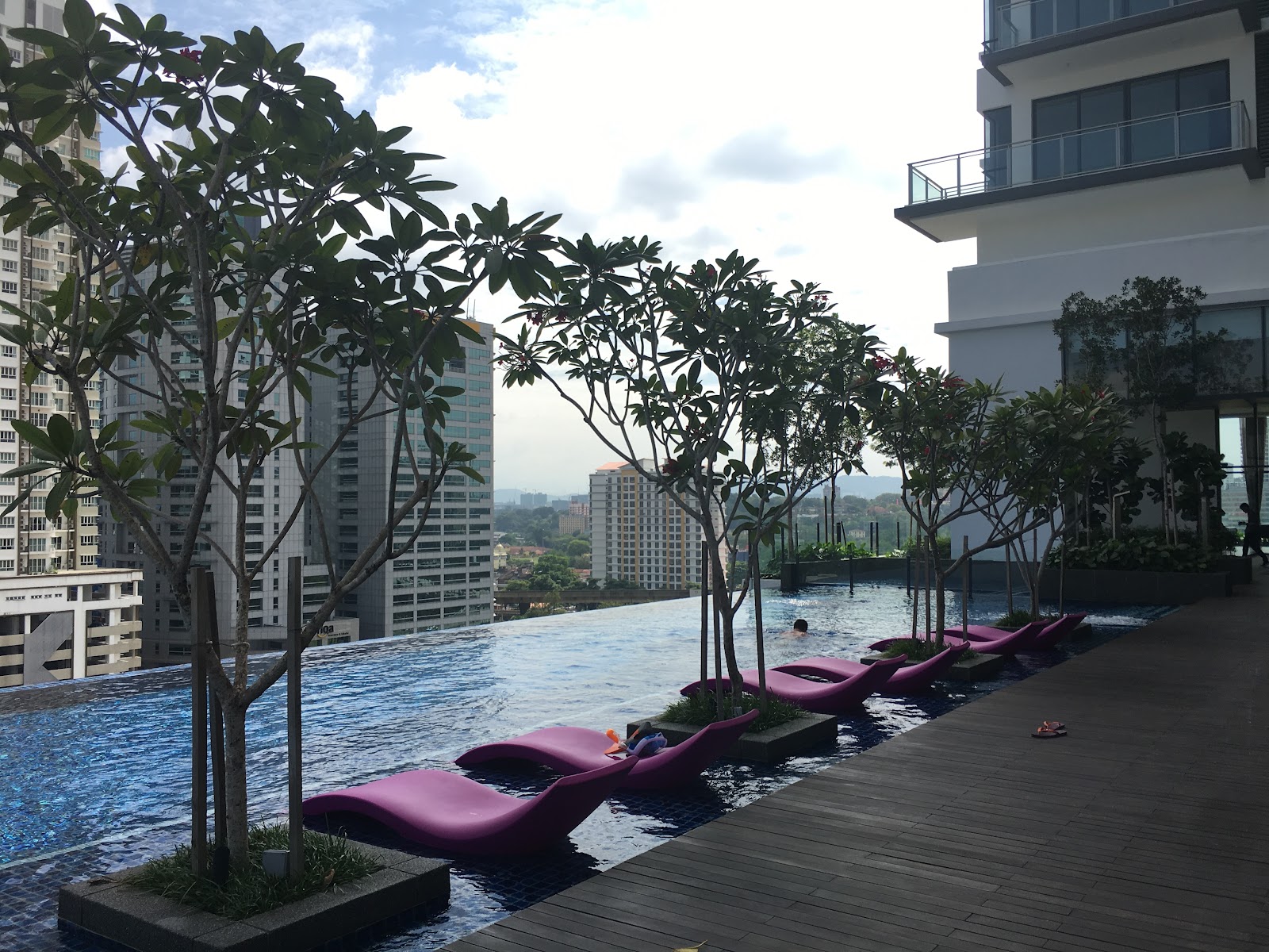 Nadi Bangsar: Rooftop infinity pool with pink lounge chairs, small trees, and city skyline view