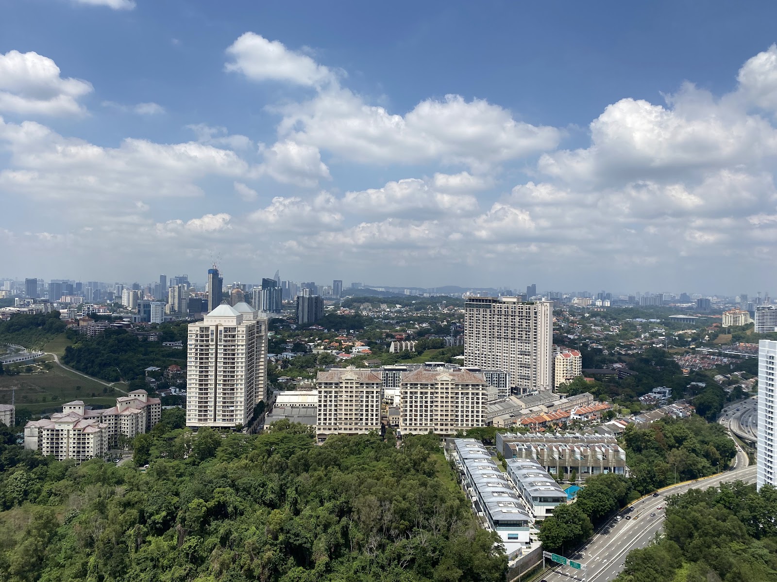 Pavilion Hilltop: Aerial view of a city skyline with high-rise towers, greenery, and roads seen from a high vantage point
