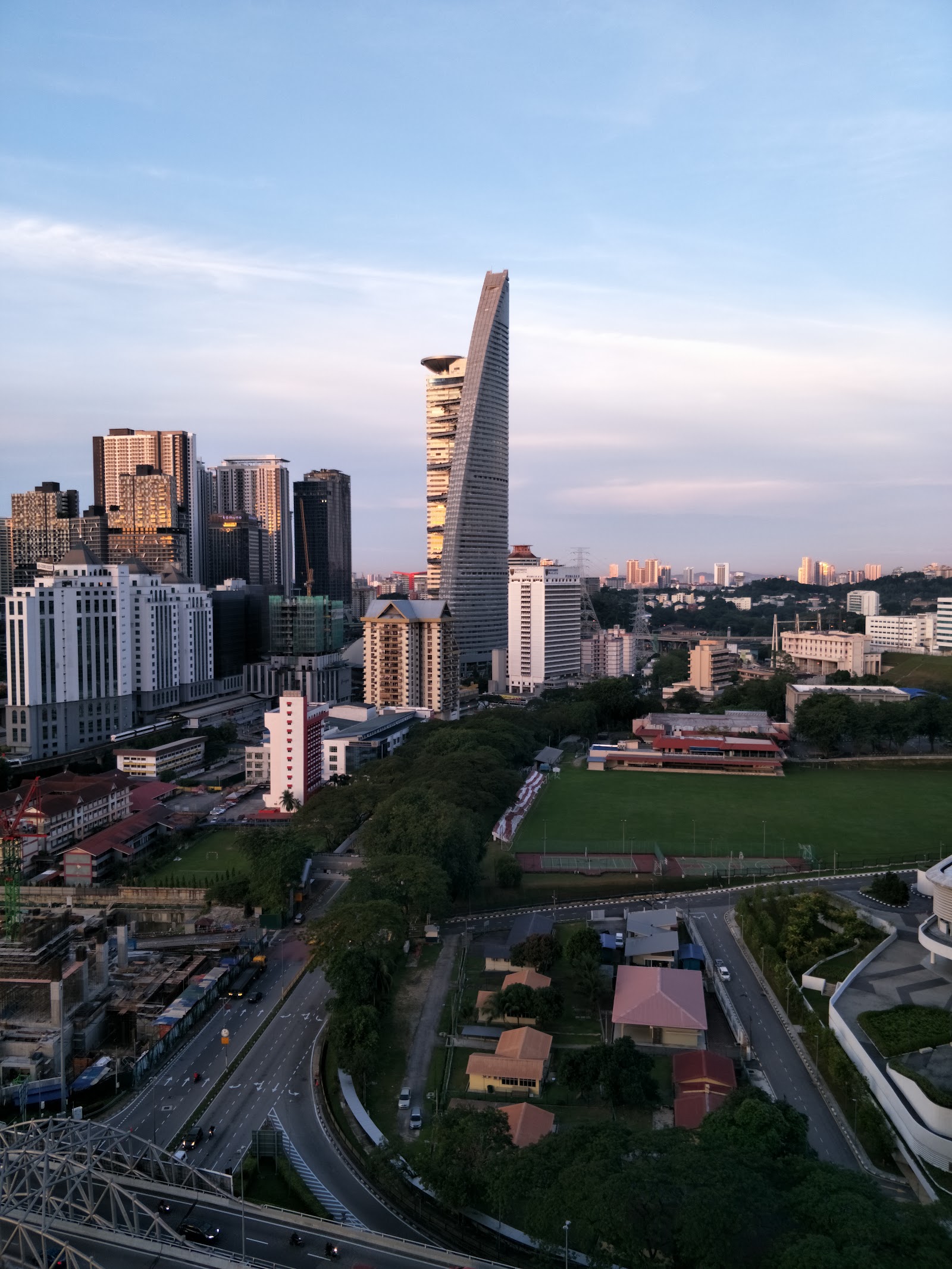 Pantai Towers: Aerial cityscape view showing skyscrapers, a football field, roads, and residential buildings under an evening sky