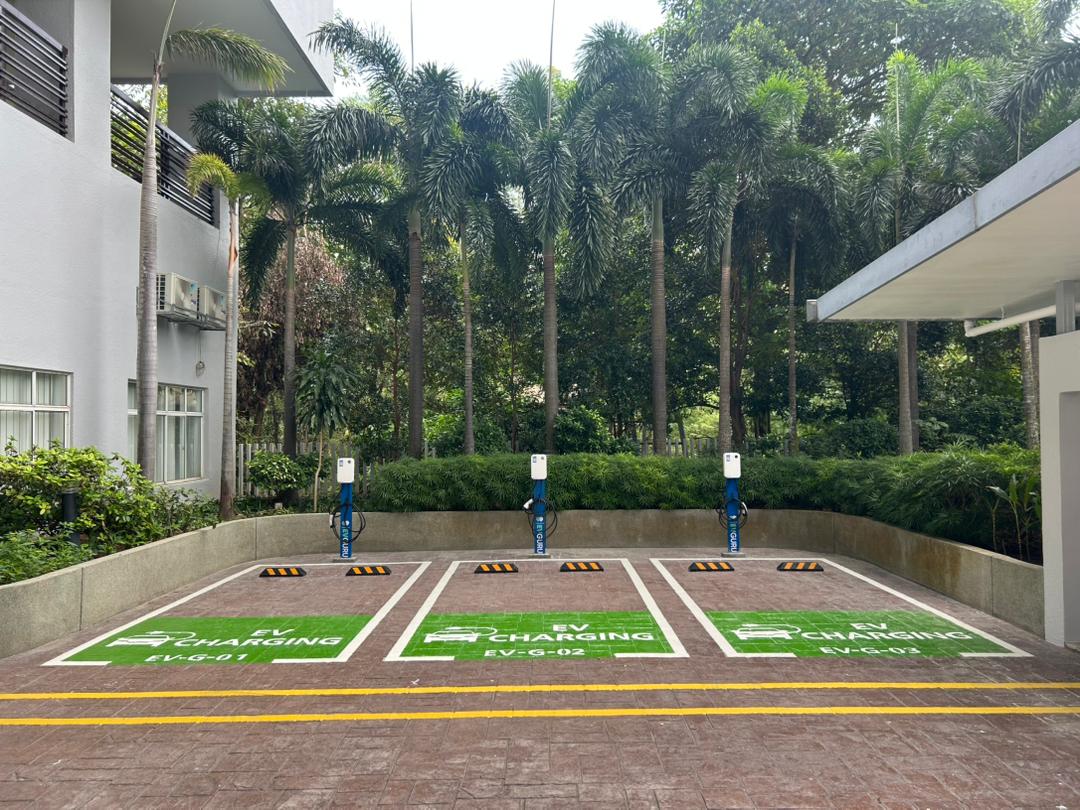 9 Bukit Utama: EV charging parking bays with three charging stations surrounded by palm trees and greenery
