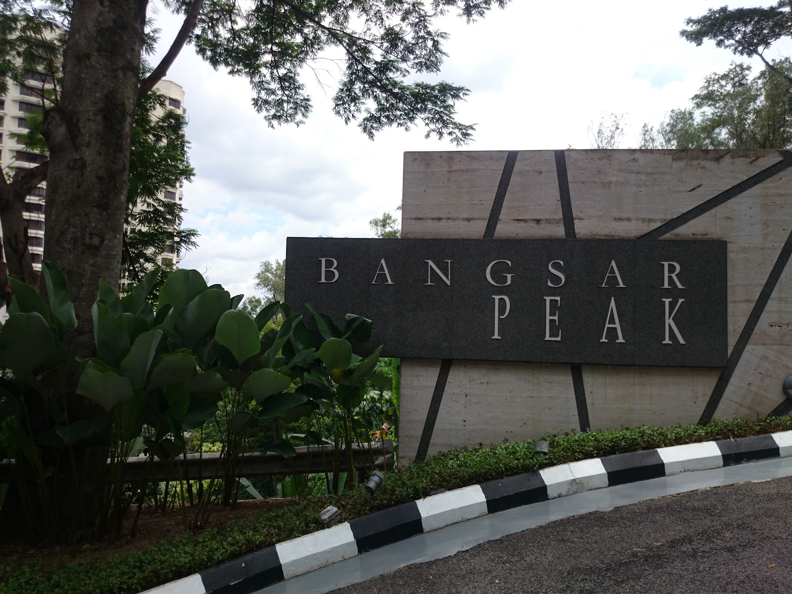 Bangsar Peak: Entrance signage for Bangsar Peak development with stone wall, greenery and a high-rise building in the background
